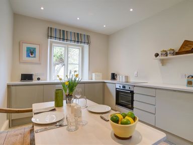 A kitchen with a table set with plates glasses and a bowl of fruit at The Old Dairy in Shilton