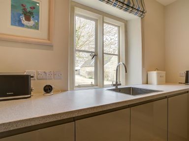 A kitchen countertop with a sink a toaster a bread box and a window with a striped roman blind at The Old Dairy in Shilton