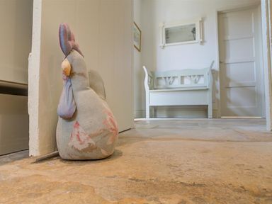 A fabric doorstop shaped like a chicken on a stone floor in a hallway with a bench and a door at The Old Dairy in Shilton
