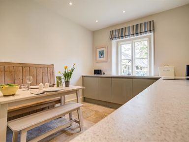 A kitchen with a wooden bench dining table set and gray cabinets under a window at The Old Dairy in Shilton
