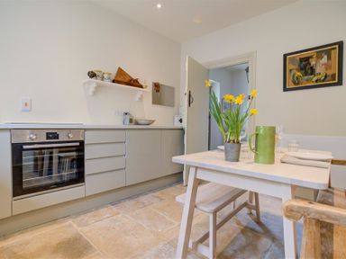 A kitchen with oven gray cabinets a wooden table with flowers and a green jug at The Old Dairy in Shilton