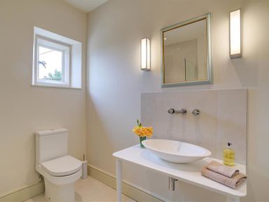 A bathroom with a toilet a white sink on a table with towels and soap and wall-mounted lights at The Old Dairy in Shilton