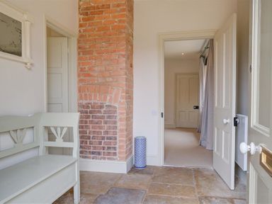 An entryway with a white wooden bench a brick column and open doors showing a hallway at The Old Dairy in Shilton