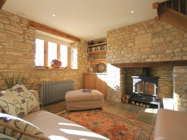 A living room with stone walls a wood stove a beige sofa and an ottoman at Calcot Peak Barn Bibury near Northleach