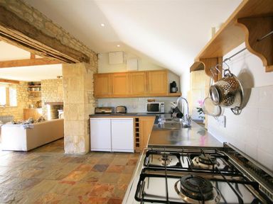 A kitchen with a gas stove and a sink next to wooden cabinets and a stone wall at Calcot Peak Barn Bibury near Northleach