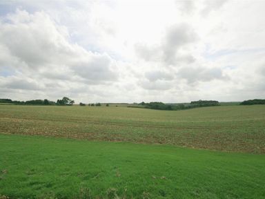 A wide view of open fields with patches of grass and trees on the horizon under a cloudy sky at Calcot Peak Barn Bibury near Northleach