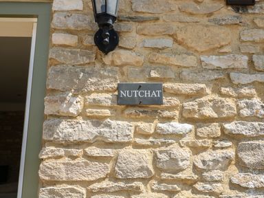 Stone wall with a black sign reading NUTCHAT and a lantern above the sign at Nutchat Barn in Burford