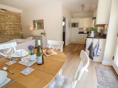 A kitchen and dining area with a wooden table set with wine glasses plates and a bottle with a stone wall on one side at Nutchat Barn in Burford