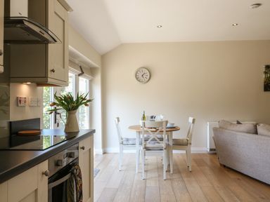 A kitchen and dining area with a small round table and four chairs near a window at Nutchat Barn in Burford