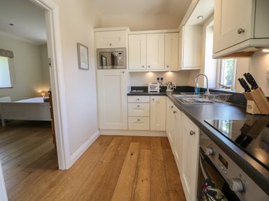 A kitchen with white cabinets black countertops a microwave toaster kettle and knives on a wooden floor at Nutchat Barn in Burford