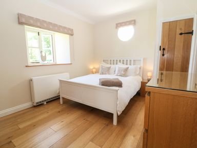 A bedroom with a white bed and floral pillows wooden floor and furniture at Nutchat Barn in Burford