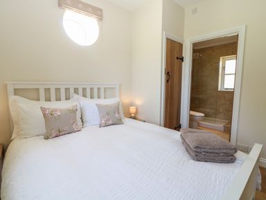 A bedroom with a white bed and floral pillows next to a door leading to a bathroom at Nutchat Barn in Burford