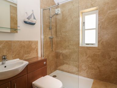 A bathroom with a shower, toilet, sink, and a small window at Nutchat Barn in Burford