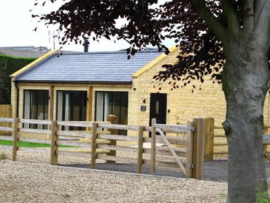 A stone house with large glass doors and a wooden fence in front at Court Hayes Farm Barns Bourton-On-The-Water