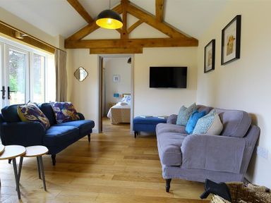 A living room with two sofas a television mounted on the wall and a view into a bedroom at Court Hayes Farm Barns in Bourton-On-The-Water