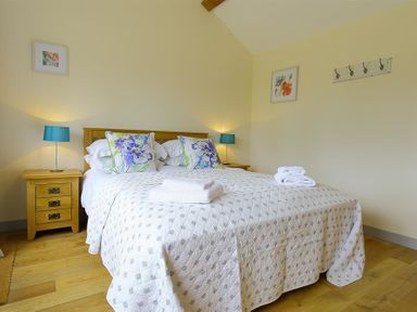 A bedroom with a double bed two bedside tables with lamps and folded towels on the bed at Court Hayes Farm Barns Bourton-On-The-Water