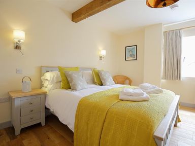 A bedroom with a bed with yellow bedding and a bedside table with a lamp at Court Hayes Farm Barns in Bourton-On-The-Water