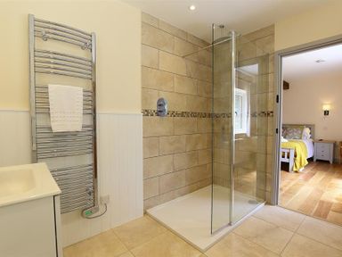 A bathroom with a glass shower enclosure and a towel radiator next to a sink at Court Hayes Farm Barns in Bourton-On-The-Water