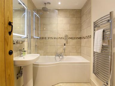A bathroom with a bathtub shower combination a sink and a towel rail at Court Hayes Farm Barns Bourton-On-The-Water