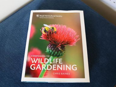 A book titled Companion to Wildlife Gardening by Chris Baines placed on a blue fabric surface