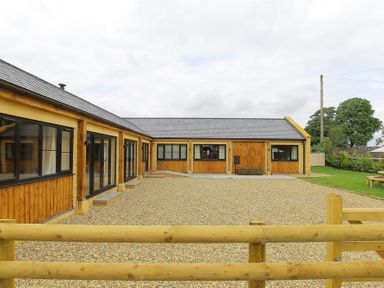 A wooden fenced gravel courtyard surrounded by single story wooden buildings at Court Hayes Farm Barns Bourton-On-The-Water
