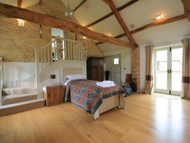 A bedroom with single bed next to wooden stairs and double doors at Stepwell in Moreton-In-Marsh