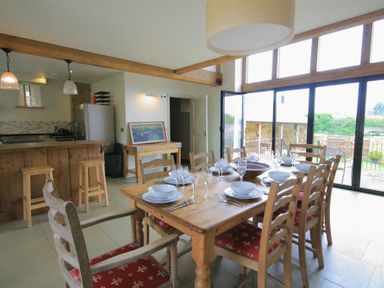 A dining area with a wooden table set for eight with bowls and glasses near a kitchen with stools at Stepwell in Moreton-In-Marsh