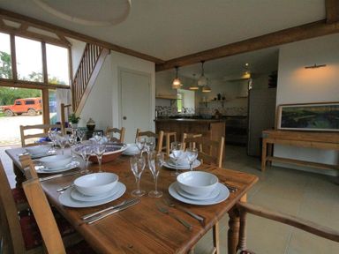 A dining area with a wooden table set with plates and glasses next to a kitchen and staircase at Stepwell in Moreton-In-Marsh