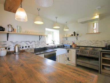 A kitchen with wooden countertop stainless steel oven farmhouse sink and shelves with kitchenware at Stepwell in Moreton-In-Marsh