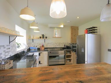 A kitchen with wooden counter black countertops stainless steel appliances and shelves with cups at Stepwell in Moreton-In-Marsh