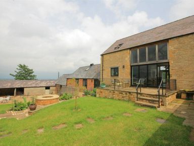 A stone house with a patio and metal railing overlooking a grassy yard at Stepwell in Moreton-In-Marsh