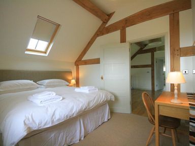 A bedroom with a double bed white bedding bedside lamp wooden desk and chair skylight window and wooden beams at Stepwell in Moreton-In-Marsh