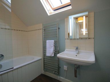 A bathroom with a bathtub a towel rack with a towel a sink and a skylight window at Stepwell in Moreton-In-Marsh