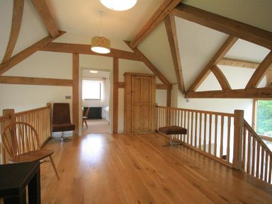 A loft area with wooden beams wooden floor two chairs a wooden cabinet and railing at Stepwell in Moreton-In-Marsh