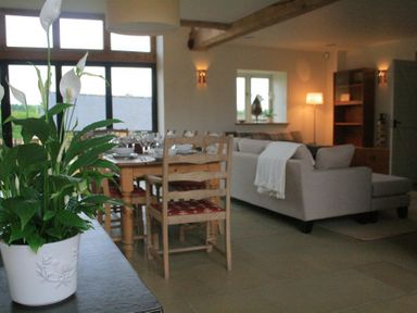 A dining table with wooden chairs and a plant on a table next to a living room with a sofa and lamp at Stepwell in Moreton-In-Marsh