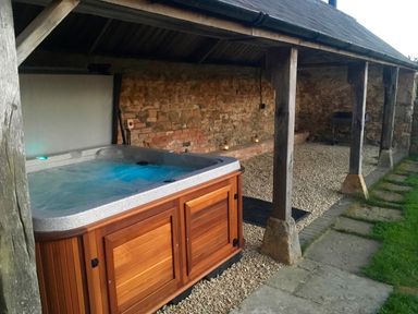 An outdoor covered area with a hot tub on a gravel floor and stone wall at Stepwell in Moreton-In-Marsh