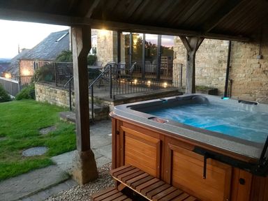 An outdoor covered hot tub next to a stone patio with metal railing and outdoor furniture at Stepwell in Moreton-In-Marsh