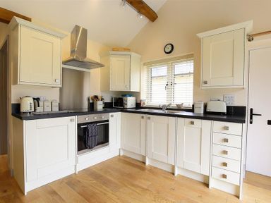 A kitchen with white cabinets black countertops and wooden floor at Park Bothy in Wyck Rissington