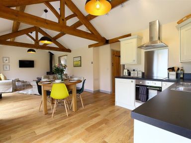 An open kitchen and dining area with wooden beams and a round table with chairs at Park Bothy Wyck Rissington