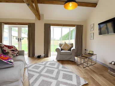 A sitting room with armchairs a sofa cushions a rug wooden floor and a wall-mounted tv at Park Bothy in Wyck Rissington