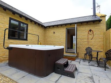 An outdoor patio area with a hot tub wooden steps and a metal table with two chairs at Park Bothy in Wyck Rissington