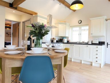 A kitchen with white cabinets a wooden dining table set with plates bowls wine glasses and flowers at Park Bothy Wyck Rissington