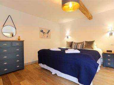 A bedroom with a bed covered by a blue blanket and white towels on top blue dressers on each side with a round mirror above one at Park Bothy in Wyck Rissington