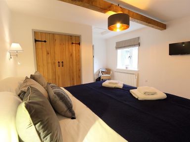 A bedroom with a bed covered by dark bedding and pillows near a wooden door and window at Park Bothy in Wyck Rissington
