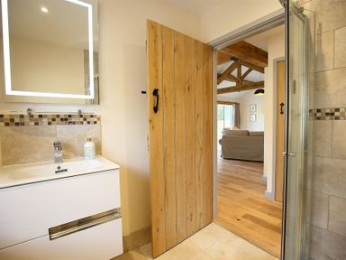 A bathroom with a sink vanity and a wooden door open to a living room with exposed wooden beams at Park Bothy Wyck Rissington