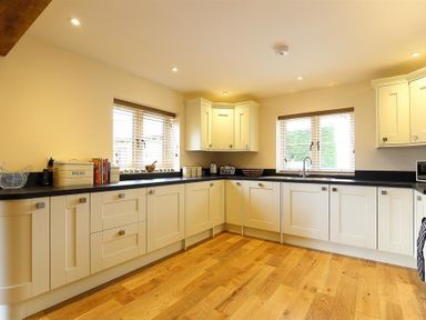 A kitchen with white cabinets black countertops wooden floor and two windows at Park Stables Wyck Beacon near Bourton-on-the-Water