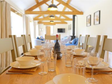 A dining table set with plates bowls glasses and a bottle in a room with wooden ceiling beams and chairs at Park Stables Wyck Beacon near Bourton-on-the-Water