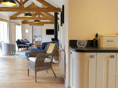 An open living area with wicker chair blue sofas wooden beams and kitchen counter with bread box at Park Stables Wyck Beacon near Bourton-on-the-Water