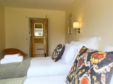 A bedroom with a double bed two patterned pillows folded towels and an open door leading to a bathroom at Park Stables Wyck Beacon near Bourton-on-the-Water