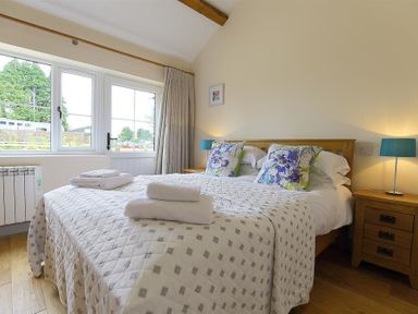 A bedroom with a double bed with folded towels on it and bedside tables with lamps at Park Stables Wyck Beacon near Bourton-on-the-Water